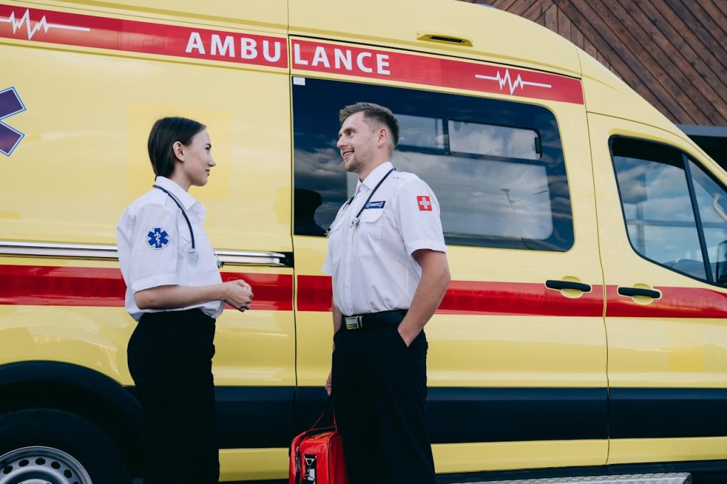 man-and-woman-having-conversation-near-an-ambulance-8942494 Two paramedics talking beside a bright yellow ambulance, showcasing teamwork and medical readiness.
